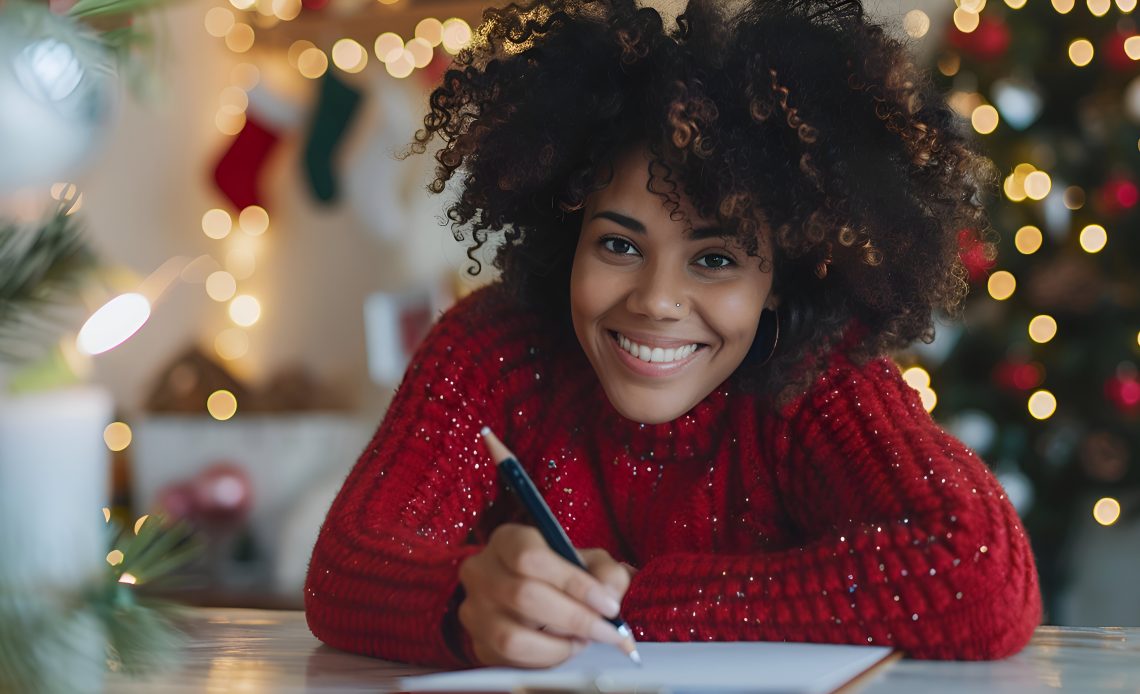 Smiling Woman in Red Cardigan Holding a pen and about writing a holiday budget